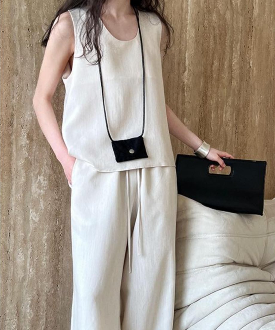 オフホワイトのノースリーブトップスとワイドパンツのセットアップを着用した女性の全身。黒いミニポーチと黒いクラッチバッグを持っている。