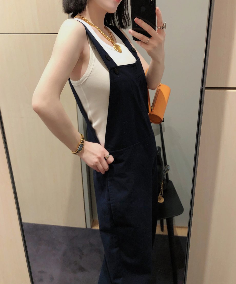 ネイビーのオーバーオールを横から見たスタイル。ゴールドのアクセサリーを身につけた女性。