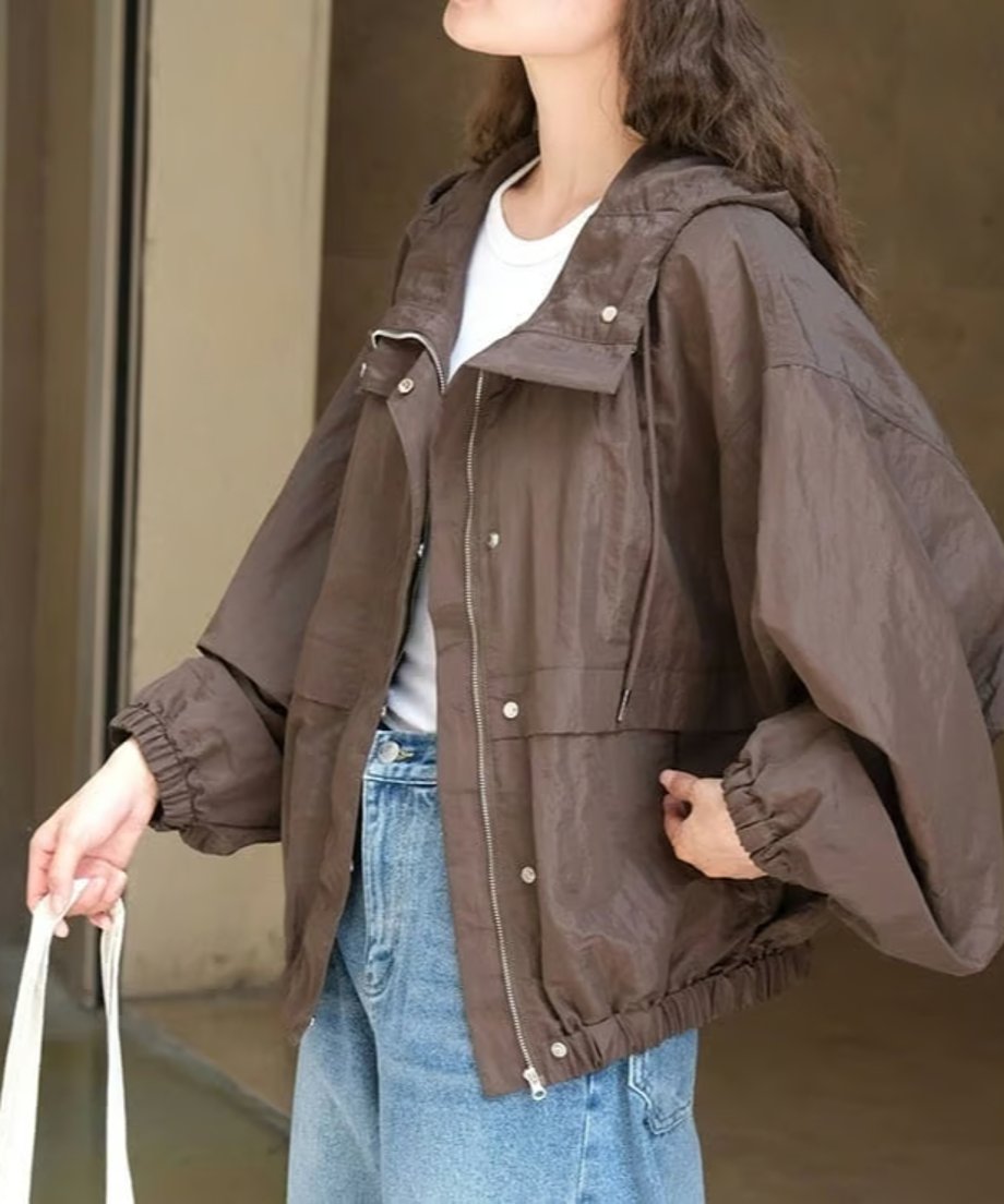 ブラウンのフードブルゾンを着用し、白Tシャツと淡いデニムを合わせた女性のバストアップ写真。白いトートバッグを持っている。