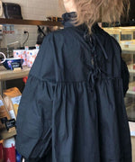 黒色のオーバーサイズブラウスを着用した女性の背中側の写真。背中の上部に複数のリボンディテールが見える。