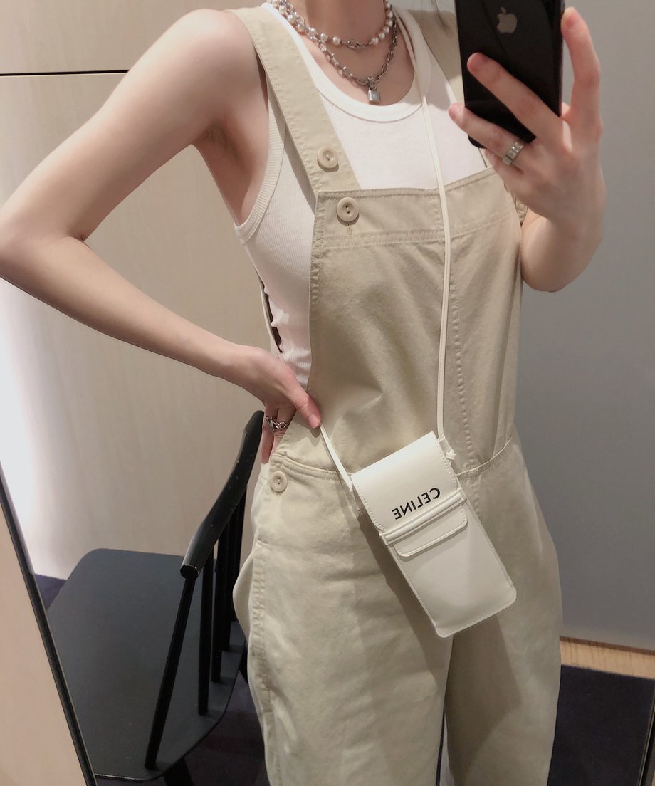 カーキのオーバーオールを横から見た女性、白いインナーとアクセサリーでコーディネート。