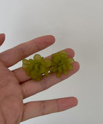 グリーンのフラワーピアスを手のひらに載せた、サイズ感と花びらの重なりがわかる詳細写真。