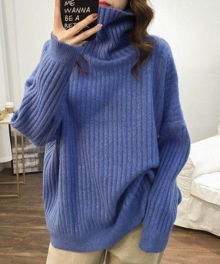 ブルーのオーバーサイズタートルネックニットを着用し、スマートフォンで自撮りをしている女性の上半身。ニットのゆったりとしたシルエットがわかる。