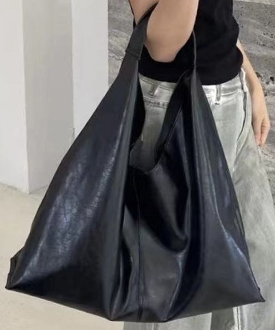 黒いTシャツとグレーのワイドパンツを着用した女性が、マットな質感の黒のソフトPU製ショルダーバッグを肘に掛けている写真。