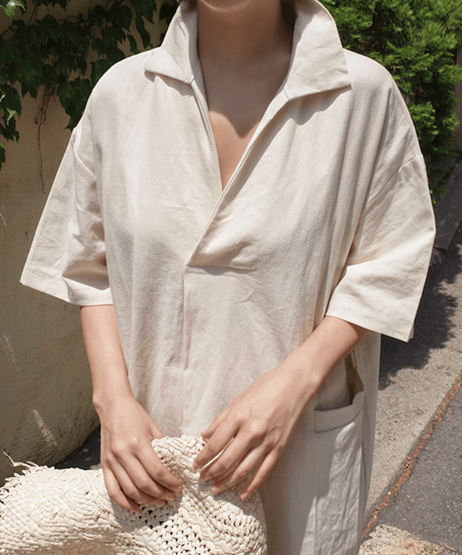 ベージュのリネン素材ドレスを着用した女性の上半身、Vネックとゆったりしたシルエットが特徴。