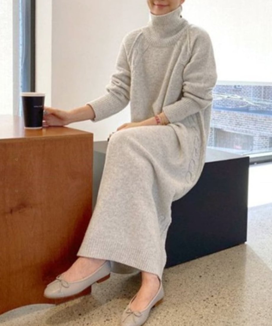 グレーのニットワンピースを着用し、椅子に座ってコーヒーカップを持った画像。