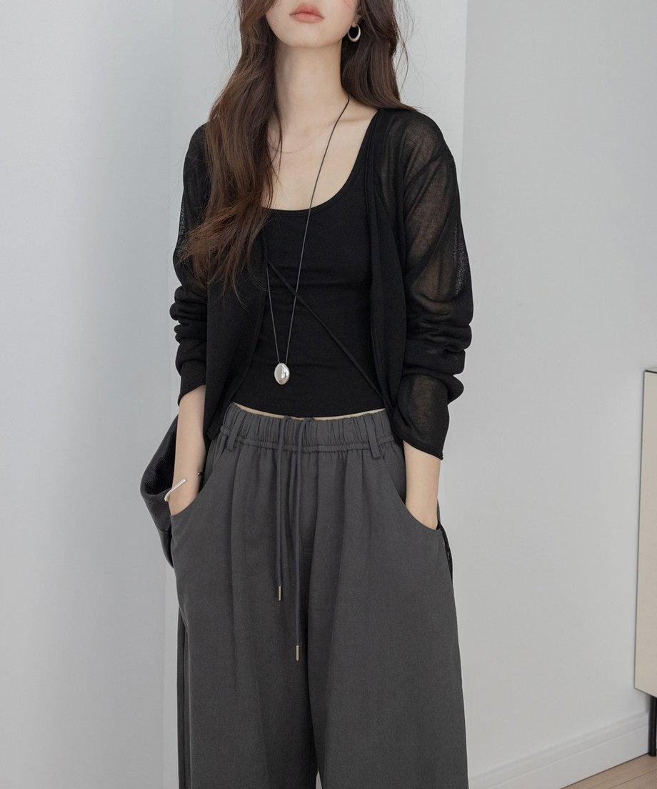 ブラックのドロストシアーカーディガンを、黒のタンクトップとチャコールグレーのワイドパンツに合わせた女性のバストアップ。長めのネックレスを着用している、洗練されたカジュアルスタイル。