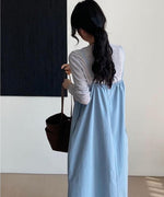グレーの長袖トップスにライトブルーのロングキャミソールワンピースを着用し、黒のトートバッグを持つ女性のバックスタイル。