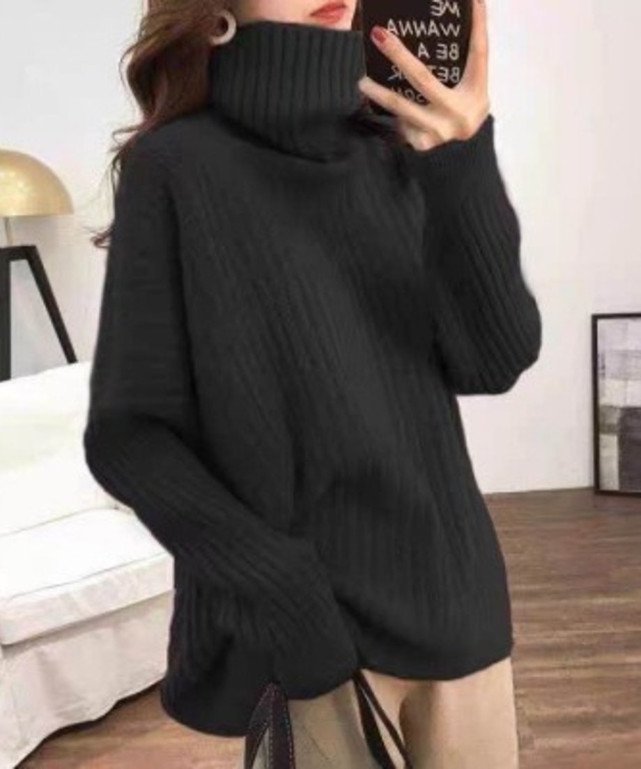ブラックののオーバーサイズタートルネックリブニットを着用し、スマートフォンを持っている女性の上半身。サイドスリットのようなディテールが見える。