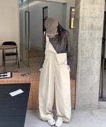 屋外の入り口付近で立ちポーズをとる女性。ベージュのワイドオーバーオールに、黒白ボーダーのシアーTシャツをインナーに、茶色のキャップと白いスニーカーを合わせている。