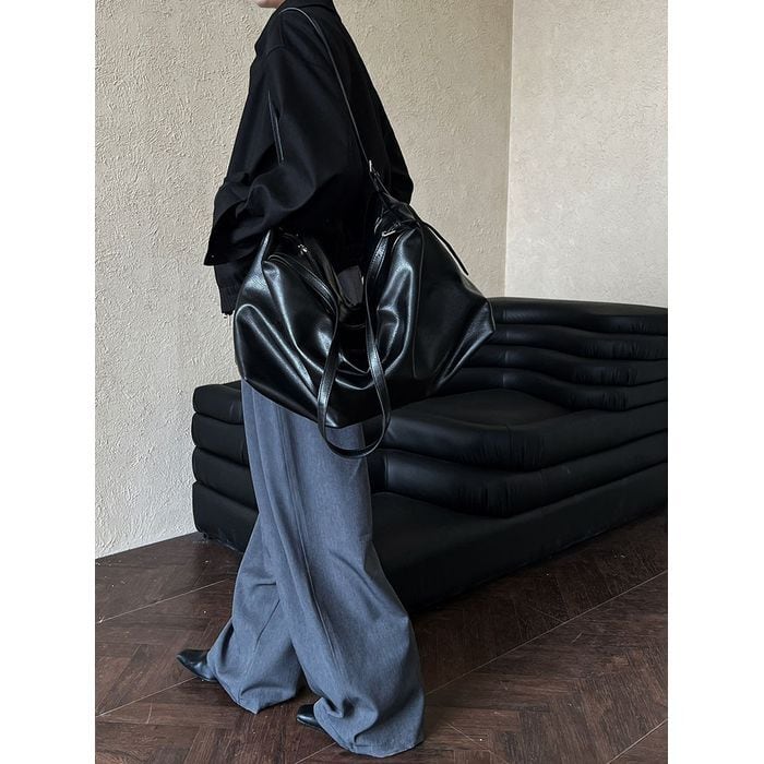 ブラックのドロップショルダーブルゾンとグレーのワイドパンツを合わせた女性の全身。大きな黒いバッグを肩にかけ、靴も黒で統一したシックな着こなし。