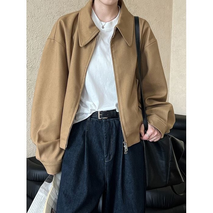 ブラウンのドロップショルダーブルゾンを着用した女性のバストアップ。インナーは白Tシャツ、ボトムスは濃紺デニム。黒いショルダーバッグを持っている。