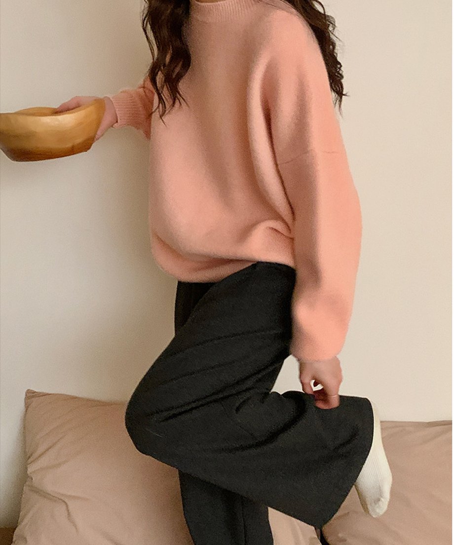ピンクのニットにダークグレーのパンツを合わせ、片足を上げて無邪気なポーズをとる全身カット。