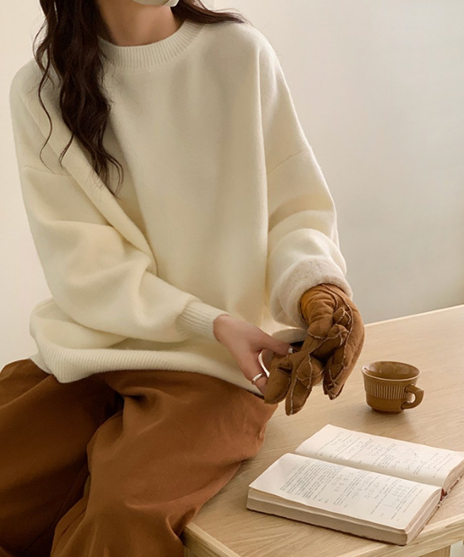 オフホワイトのニットを着てテーブルに座る女性。キャメルの手袋をはめようとしている手元のアップと、読書中の本