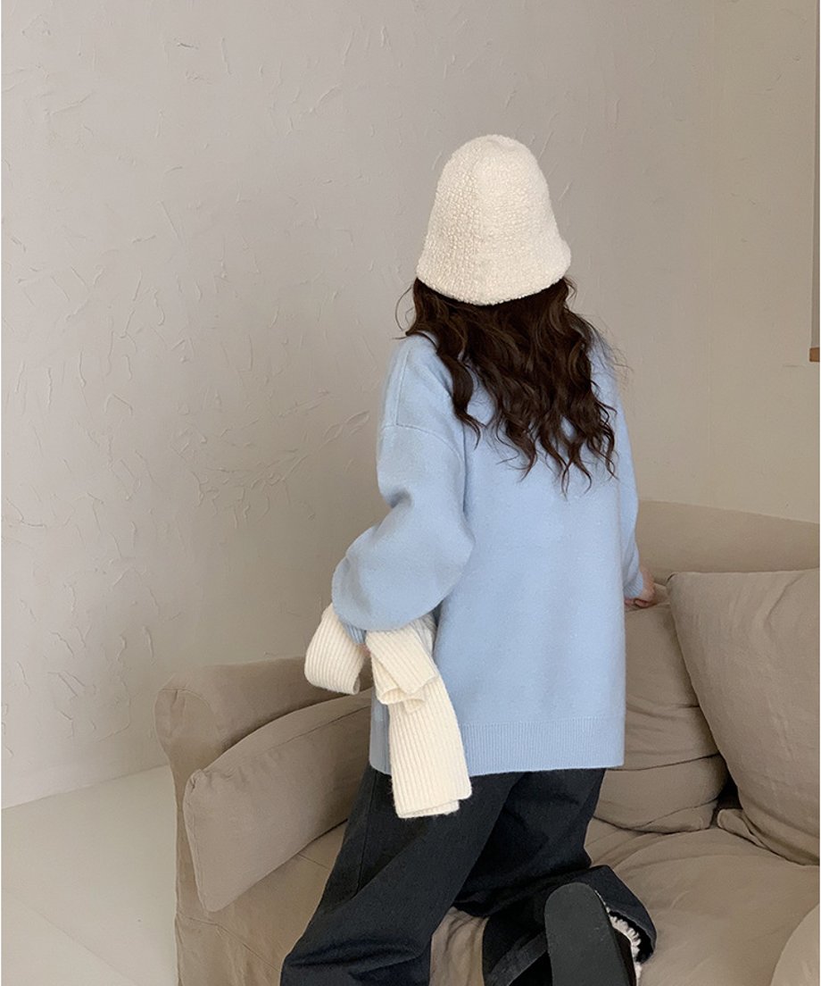 ライトブルーのニットに白いボアハットを合わせた後ろ姿。ソファに膝立ちになり、リラックスした雰囲気。