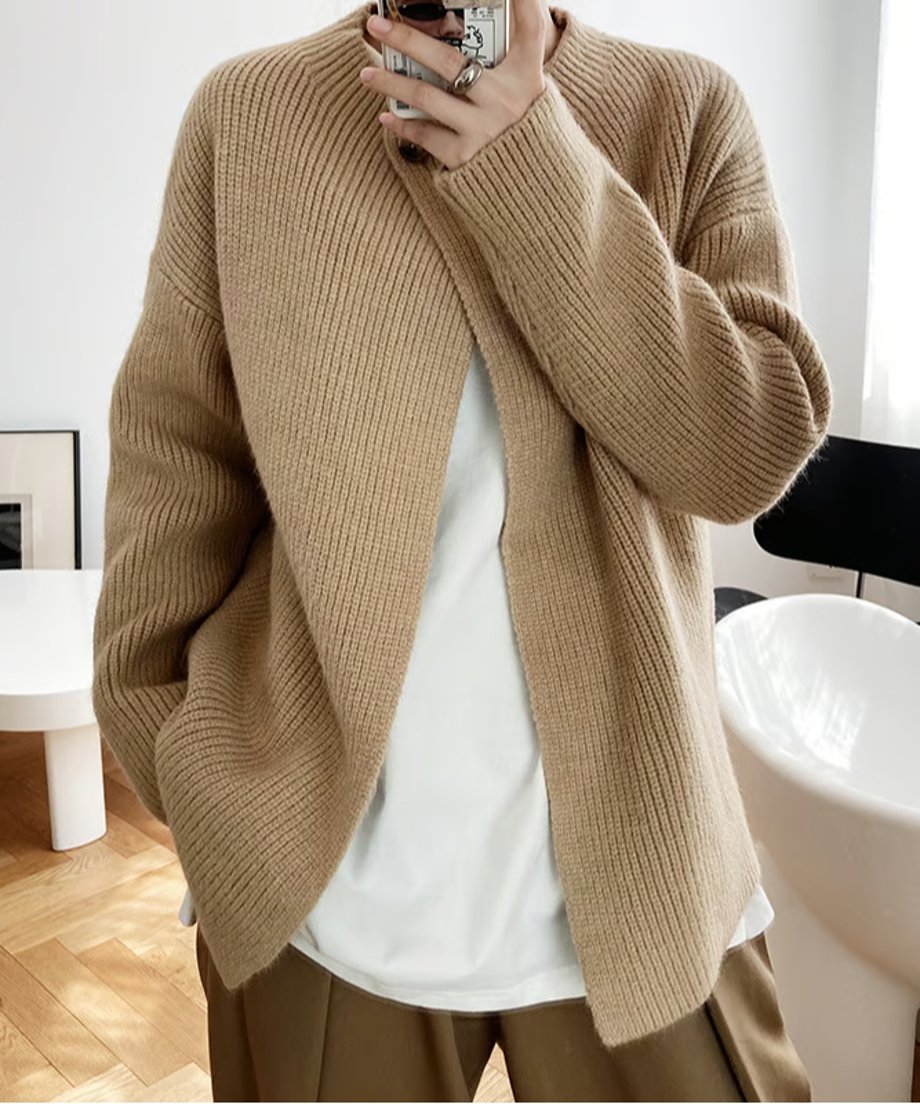 白Tシャツにキャメル色のリブ編み長袖カーディガンを着用し、携帯電話で自撮りする女性のバストアップ。