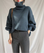 ブルーのタートルネックニットを着用した女性。ニットのゆとりのあるボリューム感とグレーのボトムスのコーディネート画像。