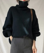 黒のオーバーサイズタートルネックセーターとグレーのパンツを合わせた半身ショット。