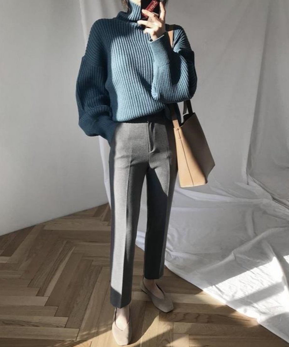 ブルーのケーブル編みタートルネックセーターを着用した全身カット。黒いパンツと合わせた落ち着いた冬のコーディネート。