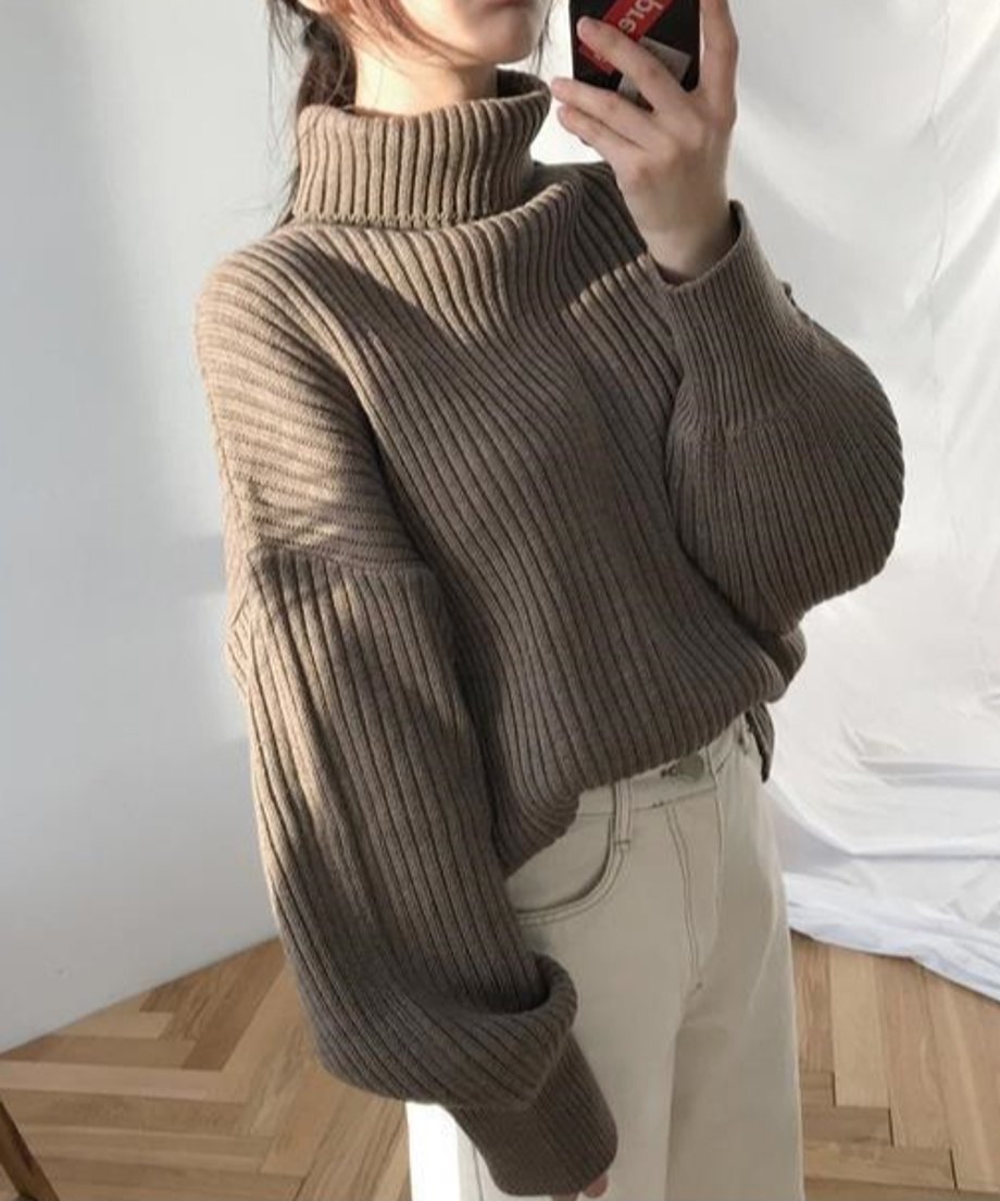 カーキのニットと白いボトムスを合わせた女性。スマホを手に持ったショット。