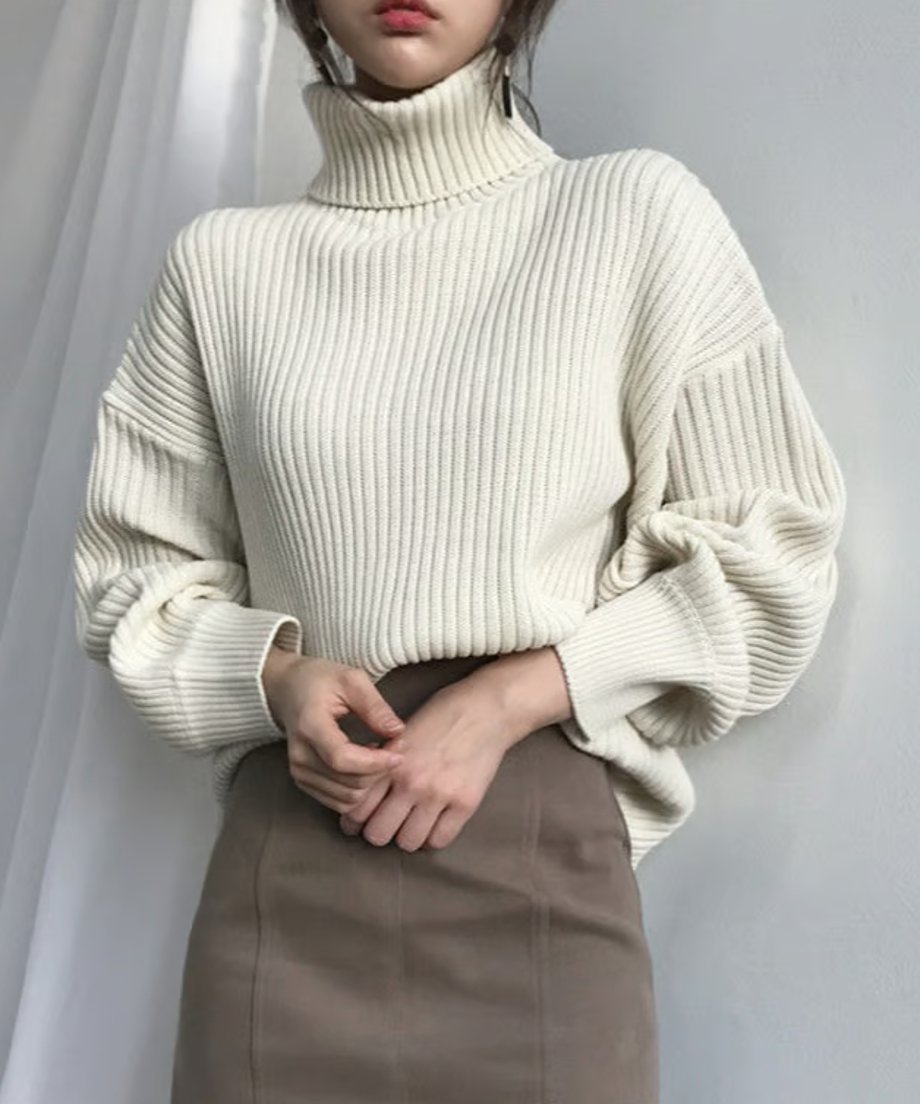 オフホワイトのニットを着用した女性がブラウンのスカートとコーディネートしている半身ショット。