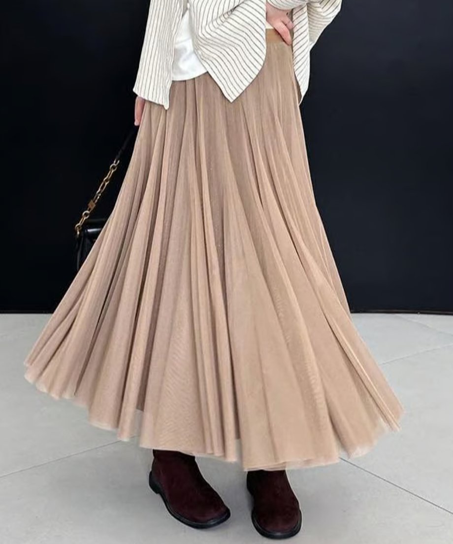 ライトブラウンのプリーツロングスカートを着用した女性の全身ショット。ストライプのトップスと茶色のショートブーツを合わせ、カジュアルながらも上品なスタイル。