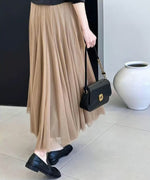 ライトブラウンのプリーツロングスカートを着用した女性のバックスタイルのショット。黒いトップスとチェーンストラップ付きの黒いバッグ、黒いフラットシューズを合わせ、洗練された大人のきれいめスタイル。