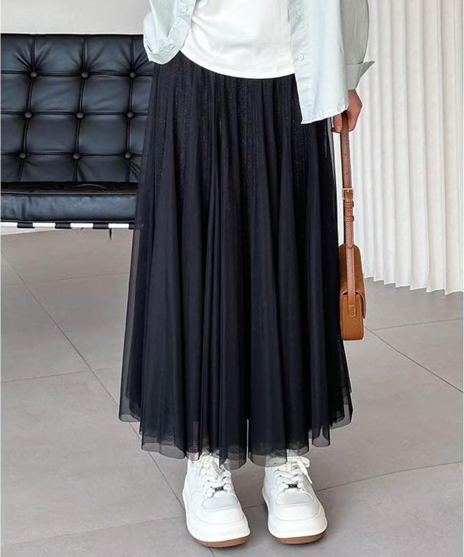 黒いプリーツロングスカートを着用した女性の、足元までのショット。白いTシャツと水色のシャツを羽織り、白い厚底スニーカーと茶色のバッグを合わせたカジュアルスタイル。