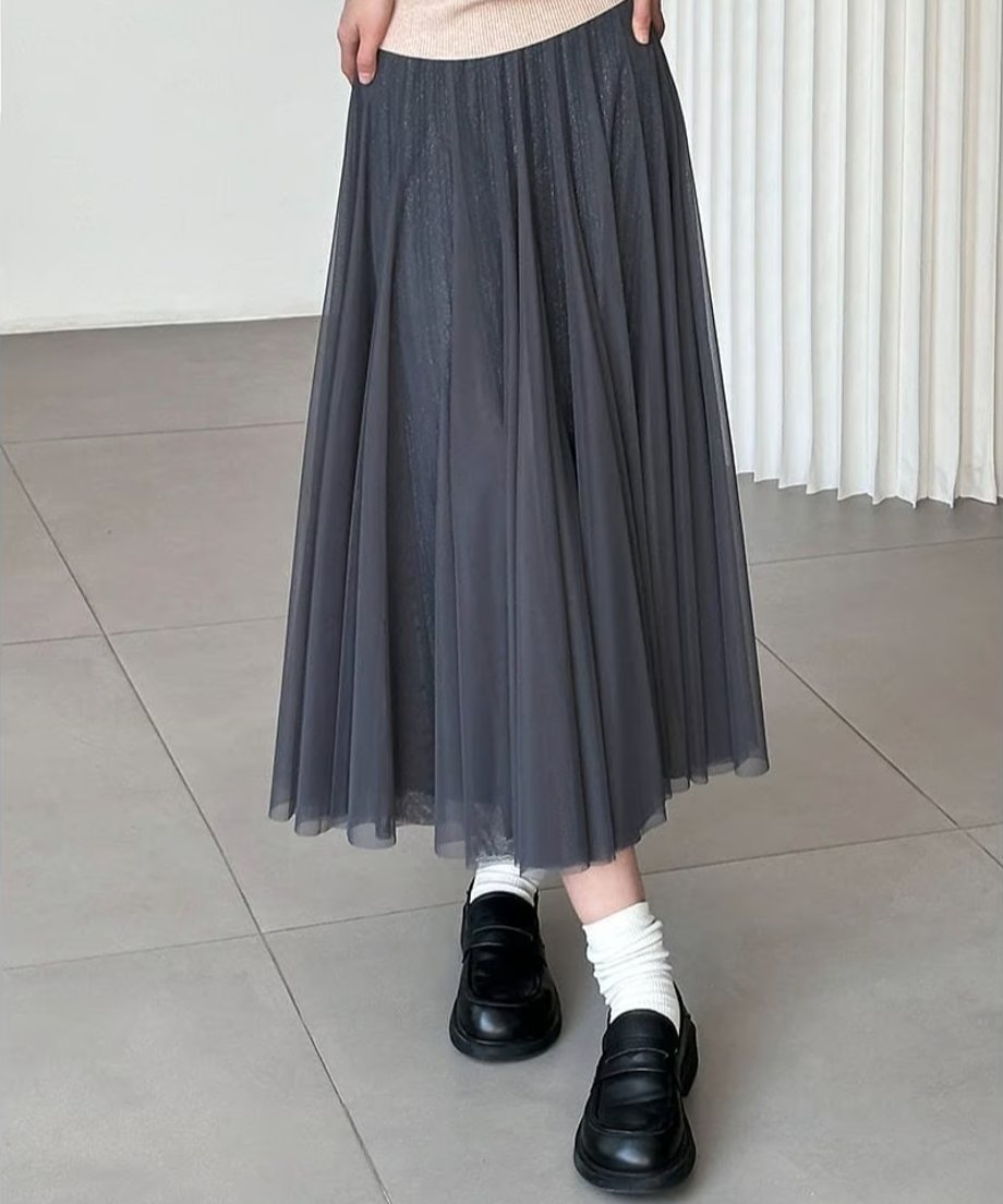 グレーのプリーツロングスカートを着用した女性の、足元までのショット。淡い色のニットに白いルーズソックスと黒のローファーを合わせた、トラッド感のあるきれいめカジュアルスタイル。