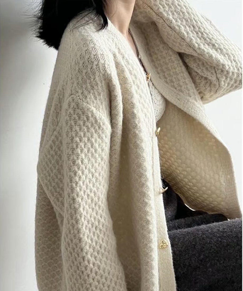 シェルホワイトのワッフル編みカーディガンを着用した女性の半身。ゴールドのハートボタンと、インナーの白のレーストップス、濃いグレーのワイドパンツが見える、上品でカジュアルな着こなし。