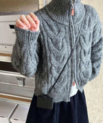 グレーのカーディガンにミニバッグを合わせた女性の半身。ハイネックの襟元と、ざっくりとしたケーブル編みの質感が強調されている。