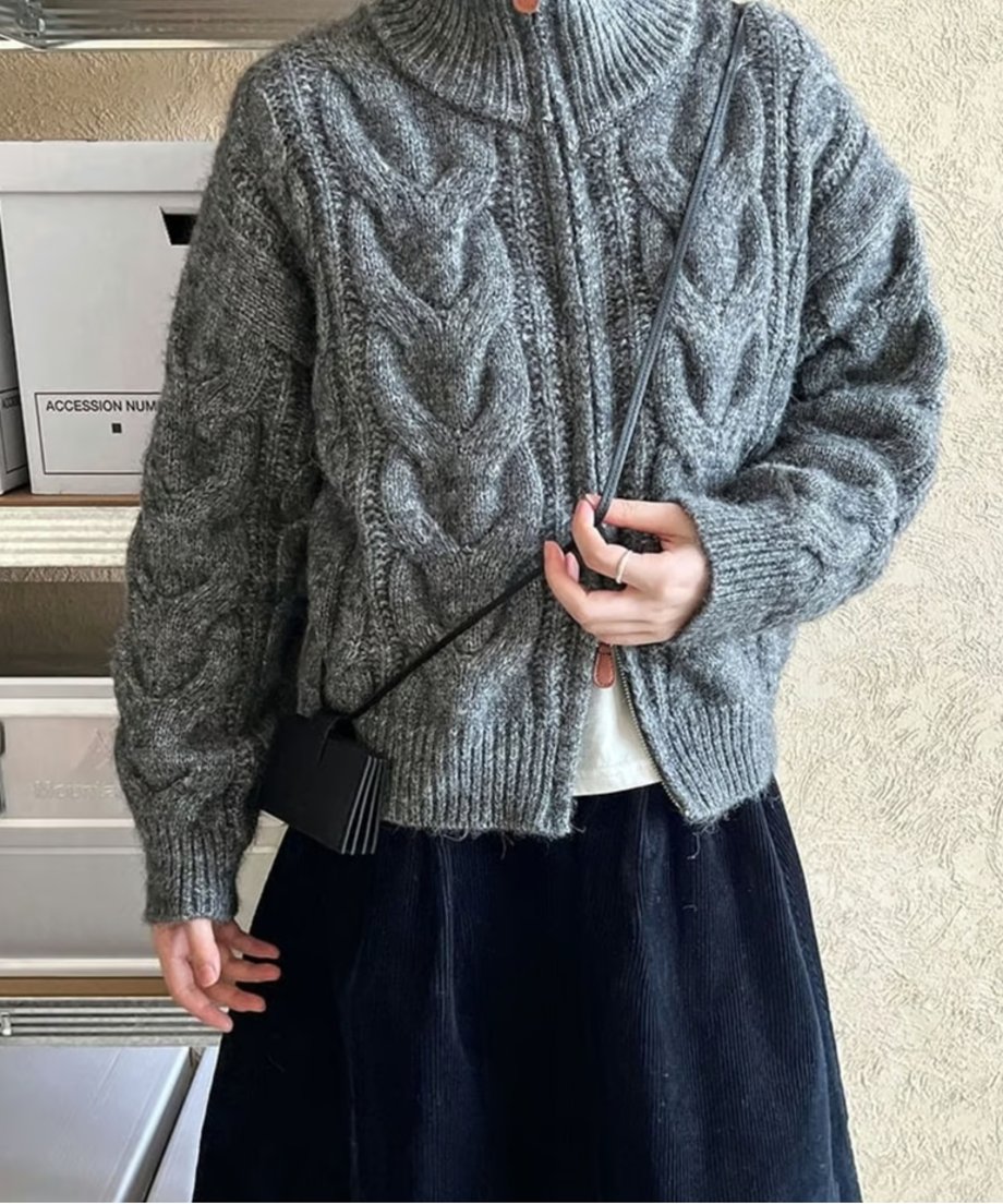 グレーのカーディガンを着用し、黒いミニバッグを斜めがけした女性の半身。スタンドカラーを少し立てた着こなし。