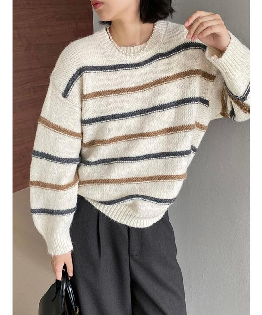 オフホワイトのマルチストライプ柄のルーズニットを着用した女性の全身画像。ゆったりとしたシルエットで、濃色とブラウンのストライプが入った秋冬のセーター。