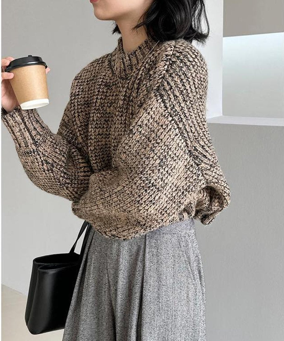 ブラウンミックスのショート丈ニットとグレーのワイドパンツを着用し、コーヒーカップを持つ人物のサイドショットのクローズアップ。