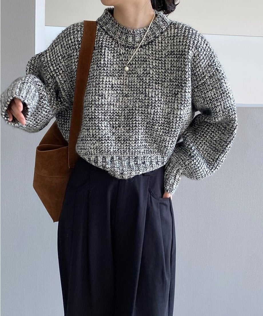グレーミックスのショート丈ニットに黒いワイドパンツを合わせ、茶色のショルダーバッグを肩にかけた人物のバストアップ。