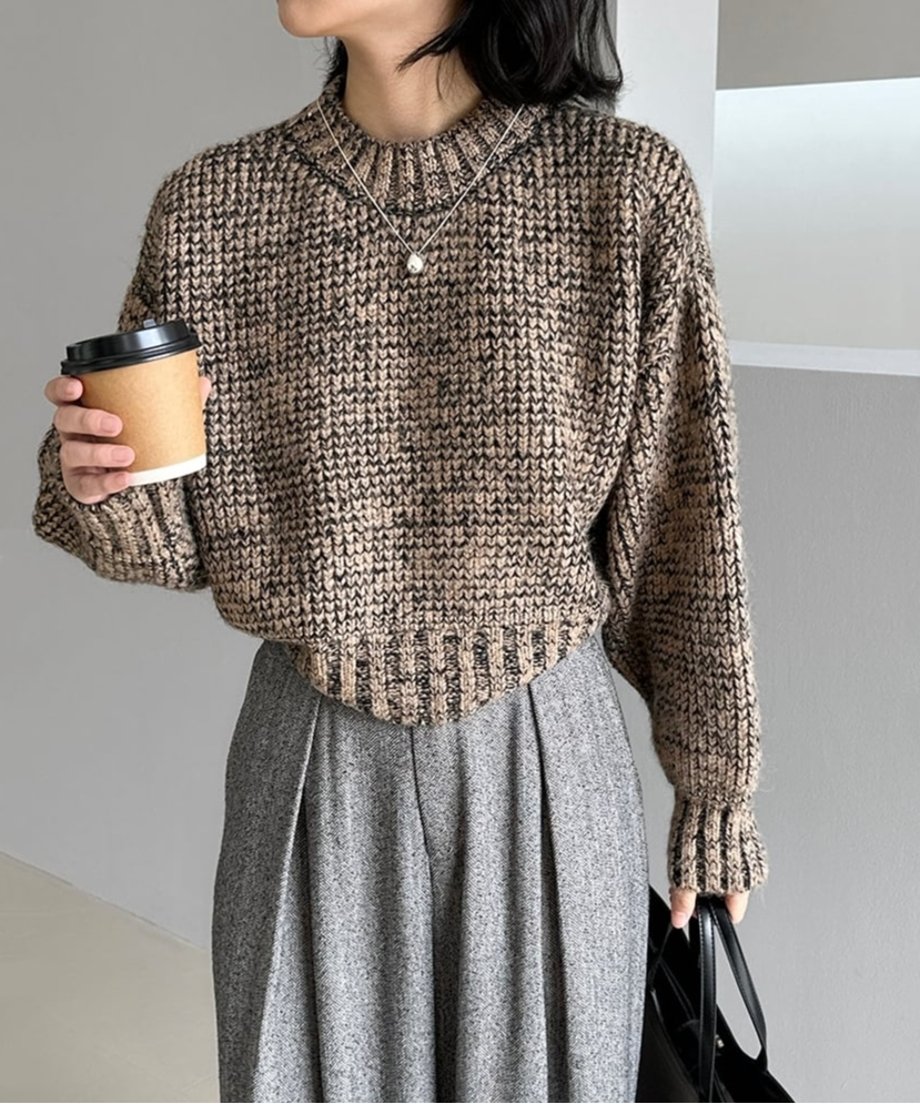 ブラウンミックスのショート丈ニットにグレーのワイドパンツを合わせ、コーヒーカップを持つ人物のバストアップ。