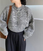 グレーミックスのショート丈ニットと黒いワイドパンツを着用し、ポケットに手を入れた人物の正面からの全身ショット。