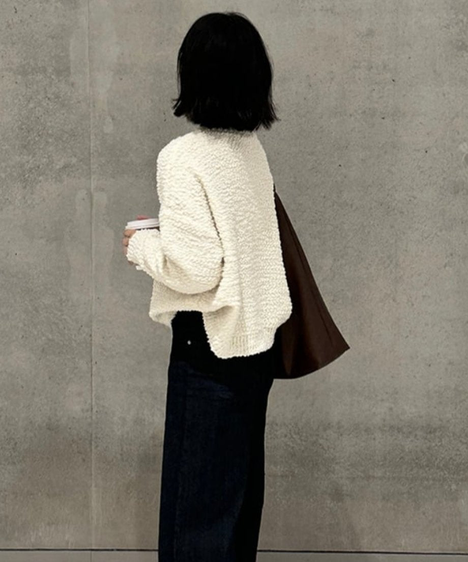 白いブークレニットプルオーバーを着用し、濃紺のボトムスを合わせた女性の後ろ姿。ゆったりとしたシルエットと、裾の前後差が確認できる。