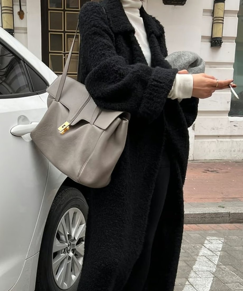 黒のロングニットカーディガンと白のタートルネック、グレーのレザーバッグを合わせた上半身のクローズアップ。