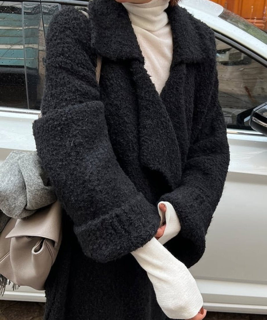 黒のロングニットカーディガンと白のタートルネックのクローズアップ。グレーのショールとバッグを手に持っており、カーディガンの質感と襟の形がよく見える。