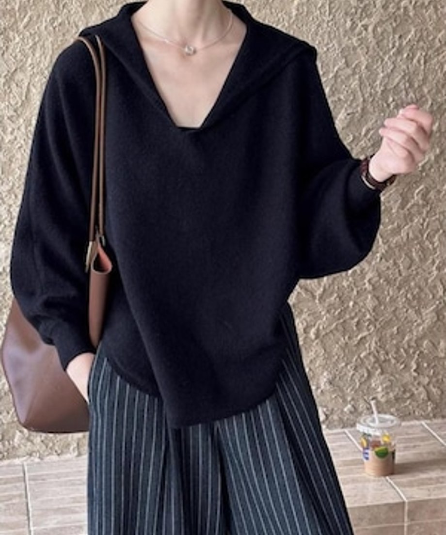 黒のセーラーカラーVネックニットと濃いグレーのピンストライプ柄ワイドパンツを着用し、茶色のバッグを肩にかけた女性のカジュアルなコーディネート。
