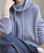 グレーのボトムスを着用し、黒いチェーンバッグを肩にかけた、グレーのルーズハイネックニットパーカーのクローズアップ。