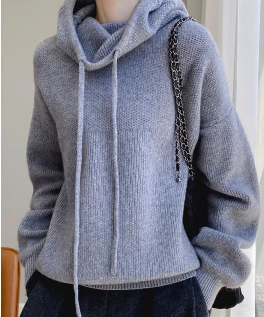 グレーのボトムスを着用し、黒いチェーンバッグを肩にかけた、グレーのルーズハイネックニットパーカーのクローズアップ。