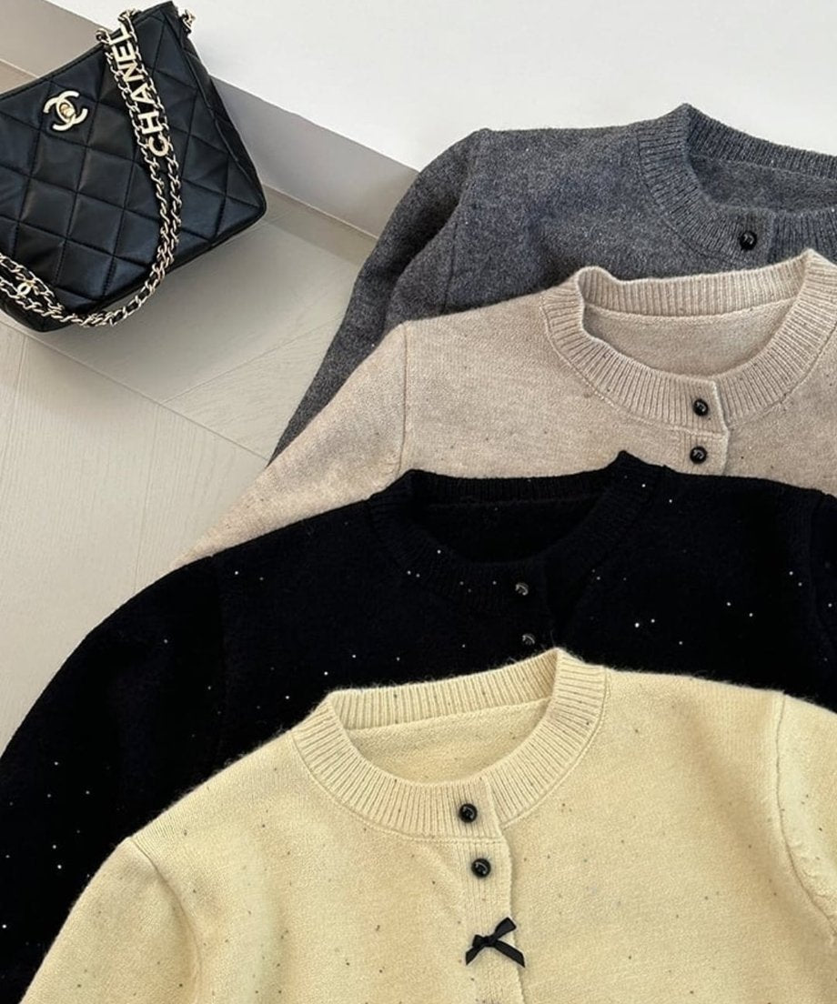 イエロー、ブラック、ベージュ、グレーの4色のリボンモチーフニットカーディガンを重ねて配置し、色展開を示した平置き写真。