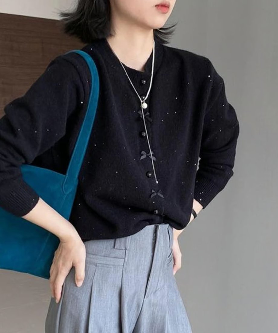 黒のリボンモチーフニットカーディガンにグレーのタックワイドパンツを合わせ、ターコイズブルーのバッグを持った女性のコーディネート。