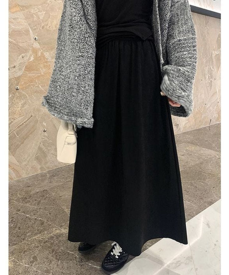 黒のロングスカートにグレーのざっくりニットカーディガンと黒のインナーを合わせたコーディネート。黒いスニーカーと白いバッグを合わせている。