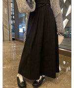 黒のロングスカートに黒の長袖トップスを合わせ、ミニバッグを持っている女性の半身像。