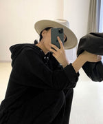 黒のボタン付きフーディとワイドパンツのセットアップを着用し、白いハットをかぶった女性の鏡越しのクローズアップ。