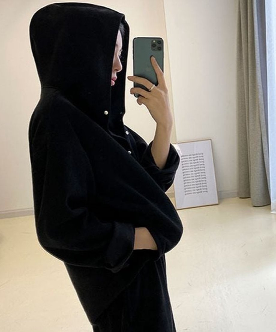 黒のボタン付きフーディとワイドパンツのセットアップを着用し、フードをかぶった女性の横顔のクローズアップ。