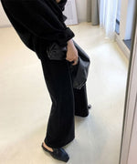 黒のボタン付きフーディとワイドパンツのセットアップを着用した女性の、上半身から足元までのクローズアップ。
